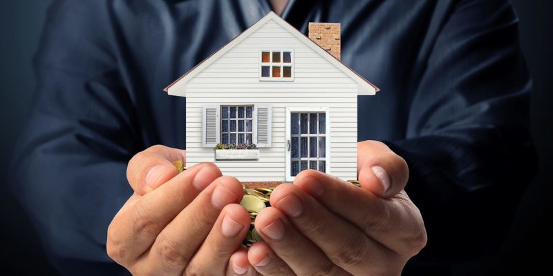 A person holding a replica of a house to give an idea of what a good cap rate for an investment property is